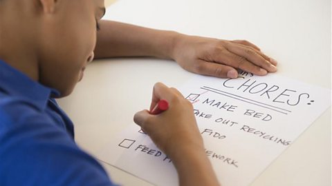 A teen boy uses a red felt-tip pen to cross an item off a list of chores.