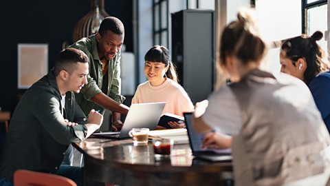 People working in a private limited company having a team meeting around a desk with cups of coffee