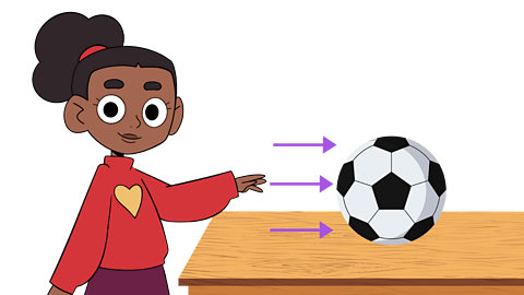 A girl pushing a football on a wooden table.