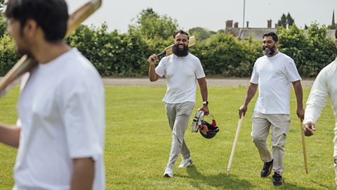 Men wearing white clothes and carrying cricket equipment.