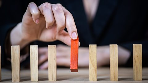 A hand picking a red stick from a line of unpainted sticks to represent target market segmentation.