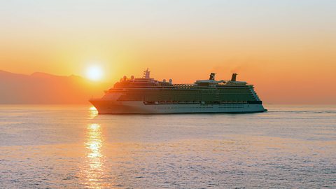 A luxury cruise ship sailing near Greece with the sun going down behind it.