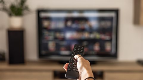 A person holding a tv remote pointing at a tv showing advertisments.