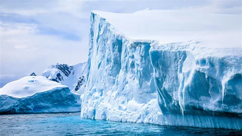 Getty Images An enormous iceberg towers over some nearby land in Antarctica (Credit: Getty Images)