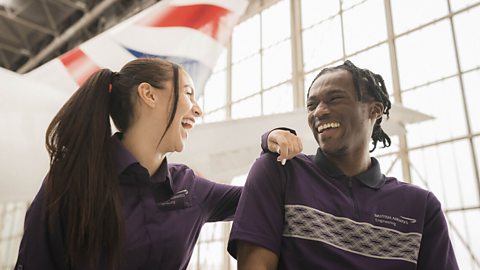 Two new employees laughing in front of an aeroplane. 
