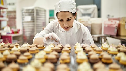 A female baker inspecting a table of cupcakes which they specialise in making