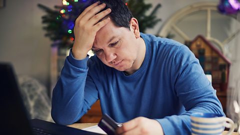 Man using a laptop to do Christmas shopping, looking stressed