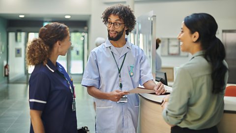 Hospital staff stand around and chat, happily. 