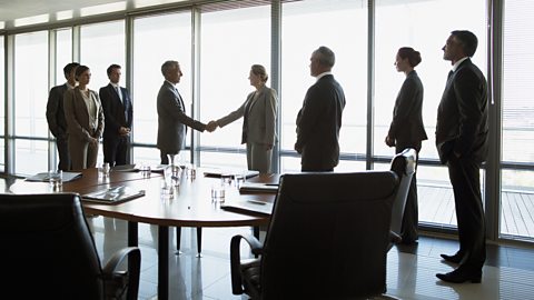 Two businesses shaking hands in a board room merger meeting.