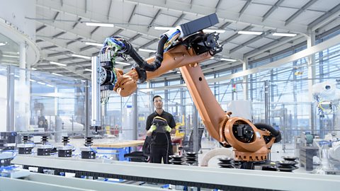 A man checking an orange robotic arm that would work in a large factory