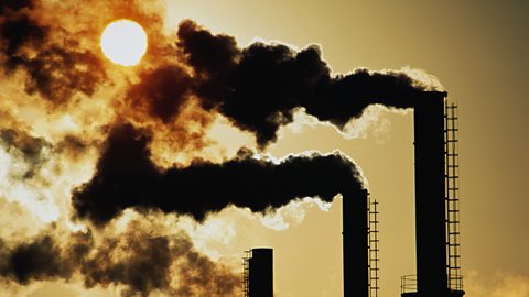 Trio of industrial chimneys emitting smoke , at sunset, the chimneys are in silhouette