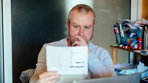 Adult man checking his bills at work. He has a worried expression and touches his face with his hand while looking at the bills.