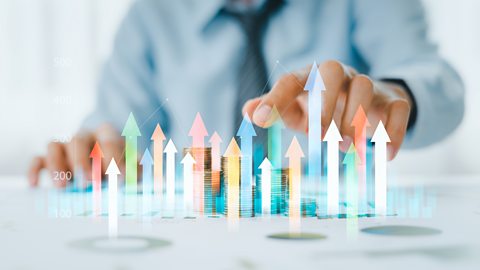 Businessman analysing trading graph financial data. Arrow of different colours are coming out of the table he is sitting at.