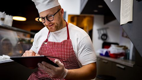 Chip shop owner looking at his accounts on a tablet.