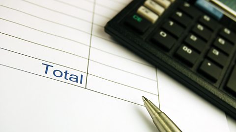 An accounts page with a blank total. There is a gold pen pointing and the black space and a black calculator.