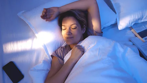 Getty Images A woman in bed with her eyes closed and arm above her head (Credit: Getty Images)