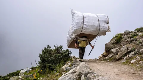 Getty Images A sherpa carrying a huge load on his back on a track in Nepal (Credit: Getty Images)