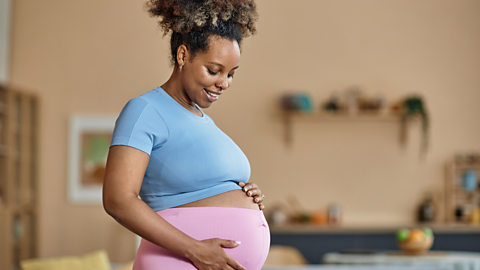 A pregnany woman in stretchy exercise clothes smiles while holding her bump