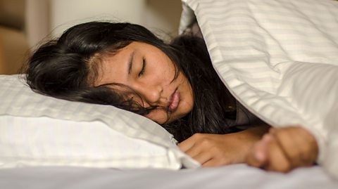 A teenager sleeping in their bed, head on the pillow, eyes closed