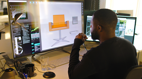 Designer working with CAD to design an orange chair with large computer screen in front