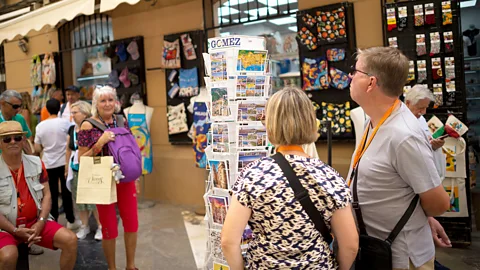 Getty Images Tourists looking at postcards outside a souvenir shop in Malaga (Credit: Getty Images)