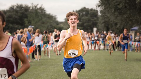 Teenage boy running to the finish line of a cross country race.