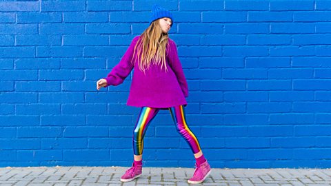 Girl dancing in front of a blue wall.