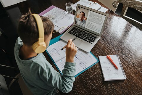 A boy sits at his desk on a web video call with a tutor for help with his home education work
