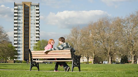 Teens sat on a bench in a park.