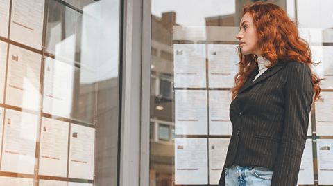 Young woman looking at windows covered with job listings.
