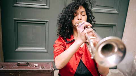 Woman playing trumpet in front of a door.