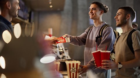 2 friends buying movie tickets and popcorn in cinema.