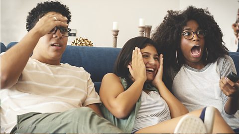 Three teenagers watching tv together on the sofa.