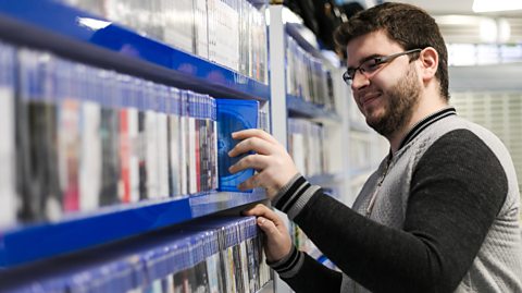 A young man pulling a videogame from a shelf in a gaming shop.
