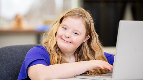 A teenage girl with Down syndrome works on her school assignments on her laptop.