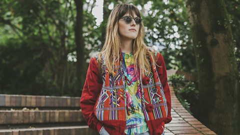 Woman wearing sunglass stood at the bottom of a stone staircase in a park.