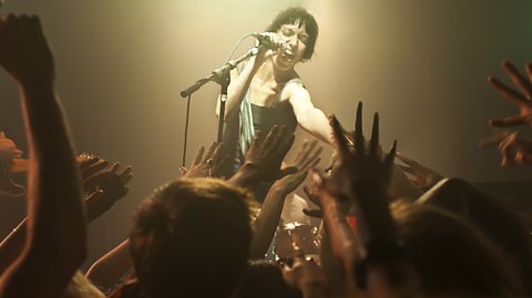 Woman singing into microphone on stage in front of crowd.