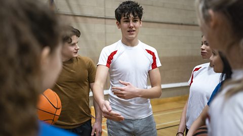 Group of students stood in a circle in a sports hall having a discussion.