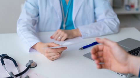 Doctor holding a prescription in their hand and a patient reaching out their hand to take it.