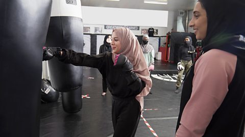 Young woman wearing hijab punching punch bag.