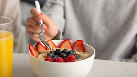 Close-up of a someone hand holding a spoon over a bowl full of fruit.
