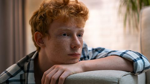 Sad boy sat on couch.