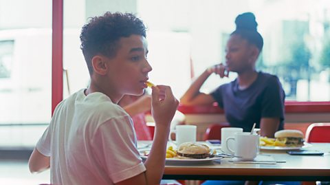 Teenage boy and girl in cafe eating burger and chips.