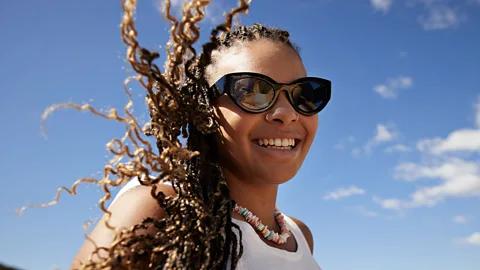 Getty Images Woman in sunglasses, a necklace and a white vest smiles (Credit: Getty Images)