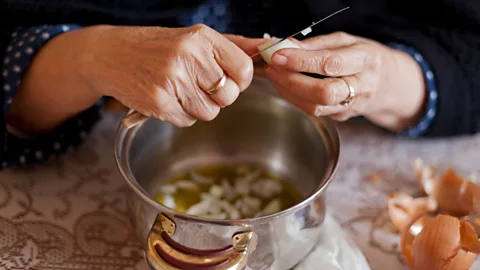 Alamy Woman's hands peeling and slicing garlic and onions with a small knife (Credit: Alamy)