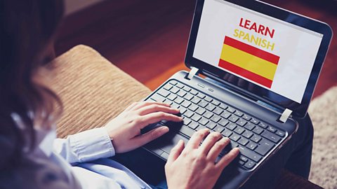 A student using a laptop to study. The screen reads ‘Learn Spanish.’ 