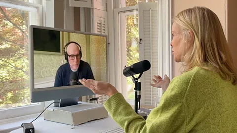BBC BBC Special Correspondent Katty Kay speaks to professor Scott Galloway via video call. She is shown from behind wearing a green jumper and using a black microphone. Galloway can be seen on Kay’s monitor wearing headphones and glasses (Credit: BBC)