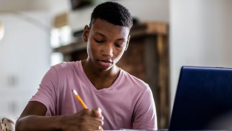 Student doing homework on a desk, holding a pencil.
