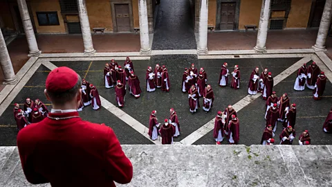 Alamy A Catholic cardinal looks down at a courtyard with many groups of cardinals in a scene from Conclave (Credit: Alamy)