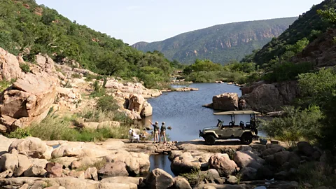 Few & Far Luvhondo People on a sustinanable game drive in South Africa with water and hills behind them (Credit: Few & Far Luvhondo)
